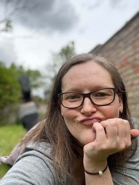 Foto, wie ich in einem Garten auf dem Bauch auf dem Gras liege, das Kinn aufgestützt und eine Schnute ziehe