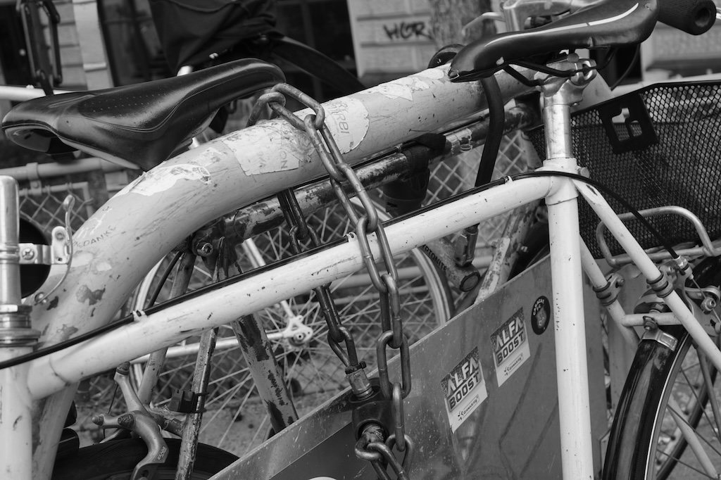 Foto einer dicken Kette, mit der ein Fahrrad an einem Fahrradständer befestigt ist.