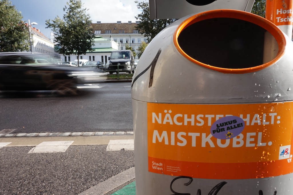 Foto eines Aufklebers "Luxus für alle" auf einem öffentlichen Mülleimer.